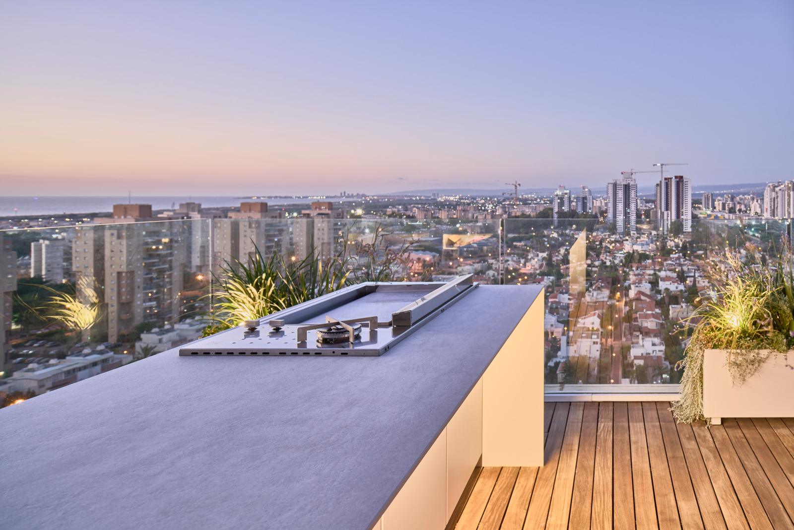 Luxury outdoor kitchen on a rooftop terrace at dusk, city skyline behind