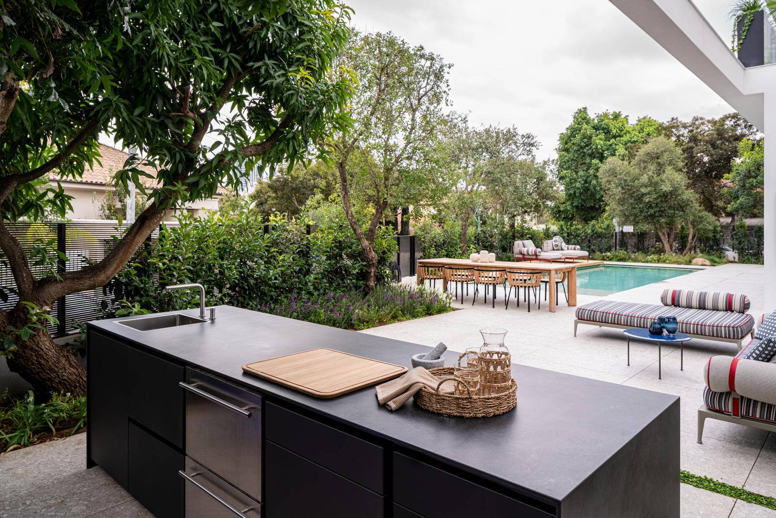 Black modular outdoor kitchen island with drawers open, showing factory-made storage modules, beside a pool